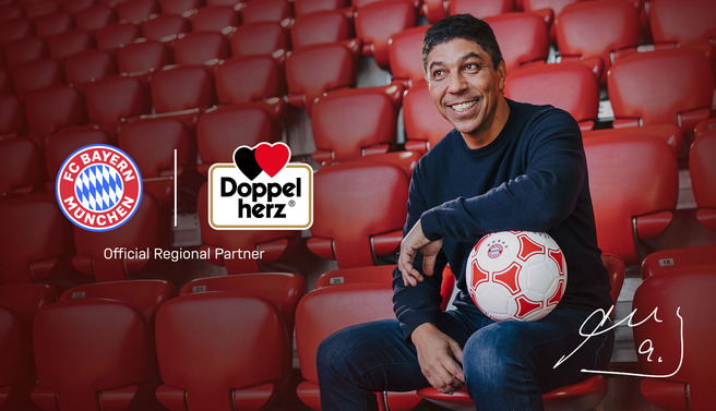 Un hombre sonriente está sentado en un estadio con asientos rojos, sosteniendo un balón de fútbol. A la izquierda, se encuentran los logotipos de FC Bayern München y Doppelherz, indicando una asociación oficial regional.