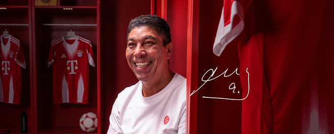 Una persona sonriente se encuentra en un vestuario deportivo rojo, junto a camisetas de un equipo de fútbol. El ambiente es cálido y acogedor, con una pelota de fútbol visible. La imagen transmite alegría y camaradería.
